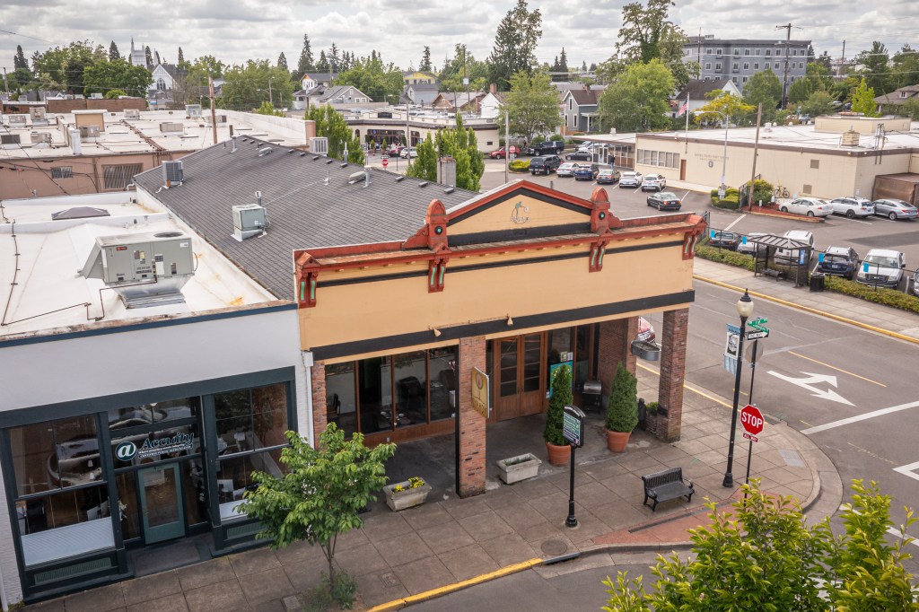Low aerial of front of tan building and white building attached on the left